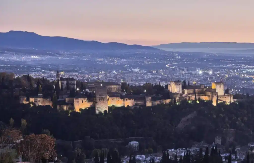 La Alhambra iluminada de noche bajo un cielo de atardecer vista desde el barrio del Albaicín.