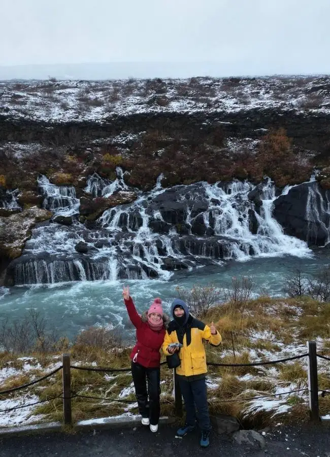 Pareja posando con ropa de invierno frente al salto de agua de Hraunfossar.