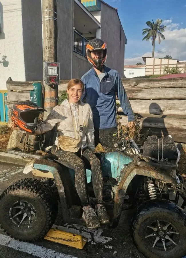 Pareja montada en un quad (cuatrimoto) cubiertos de barro tras la aventura hacia Tochecito.