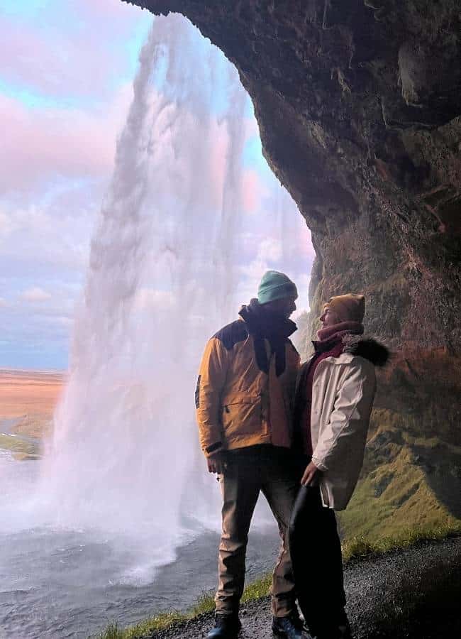Pareja de viajeros posando juntos detrás del salto de agua de Seljalandsfoss durante el atardecer.