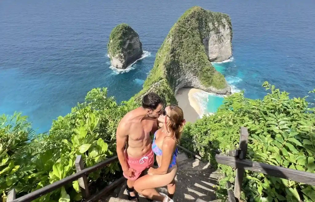 Pareja abrazada en el mirador de Kelingking Beach con el acantilado al fondo.