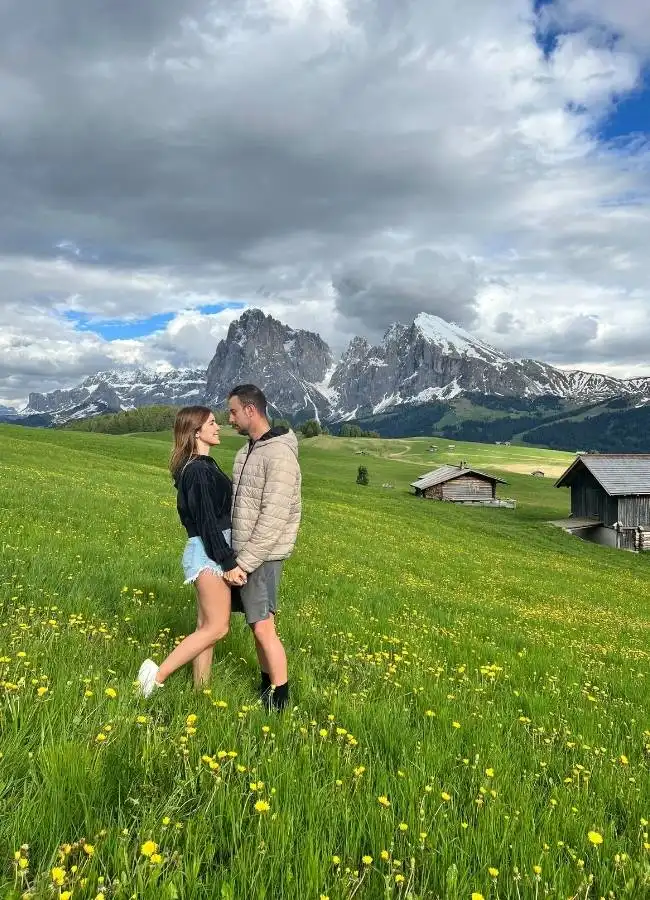 Pareja de la mano caminando por una pradera alpina en un día soleado.