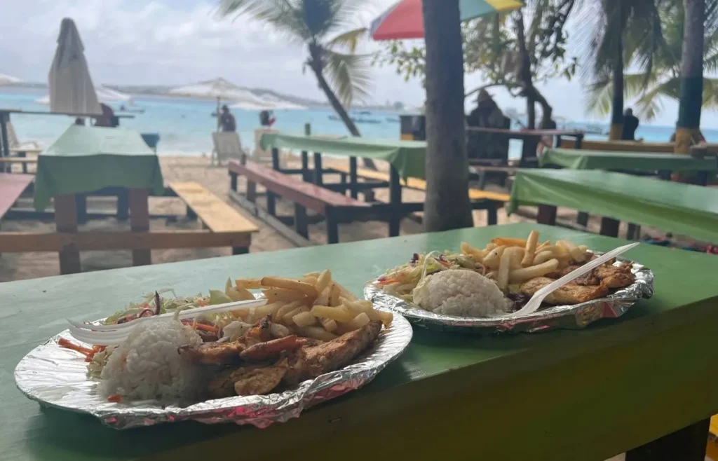 Platos de comida tropical en mesa junto al mar.