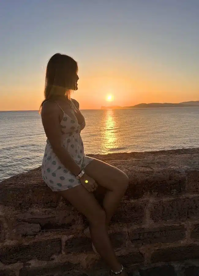 Mireia sentada en las antiguas murallas de Alguero durante la puesta de sol en Cerdeña.