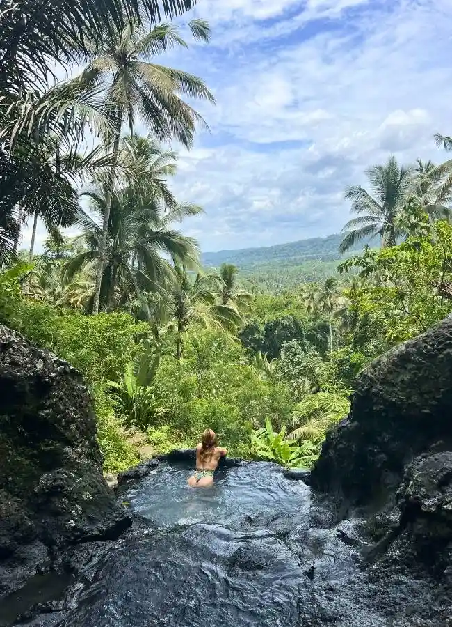 Mujer en piscina natural con vistas a jungla tropical.