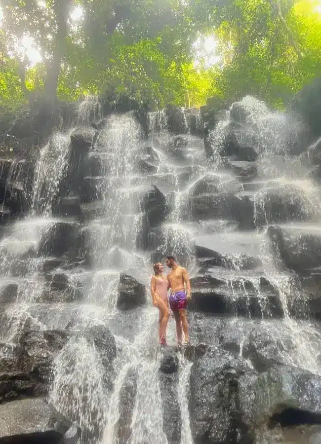 Viajeros con ruta posando en las rocas de una impresionante cascada escalonada en Bali, Indonesia.