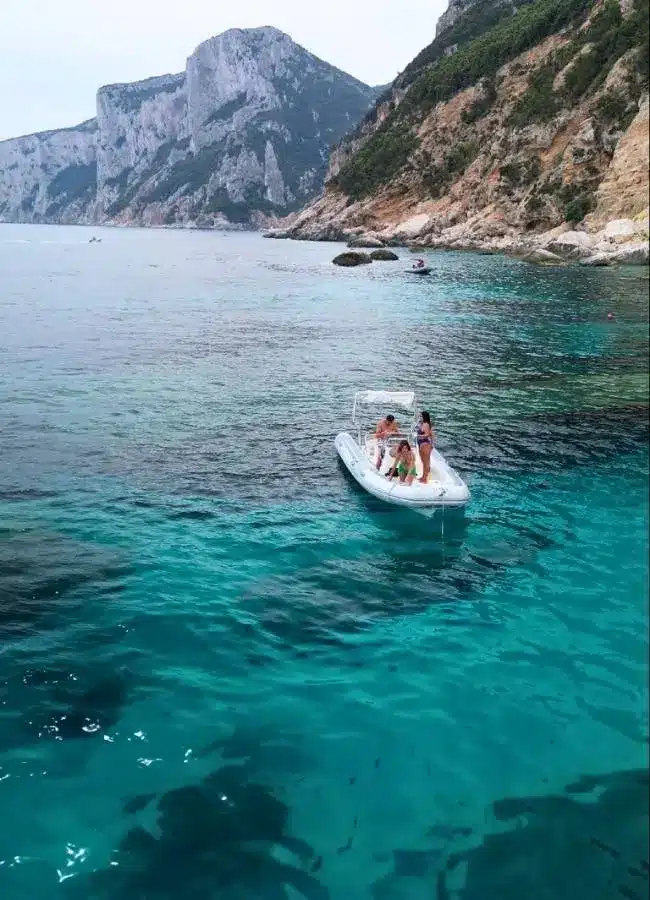 Una pequeña lancha motora navegando junto a los grandes acantilados de la costa este de Cerdeña.