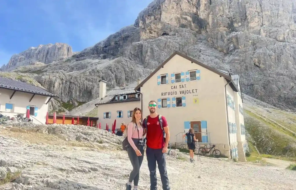 Pareja senderista frente a refugio de montaña en los Dolomitas.