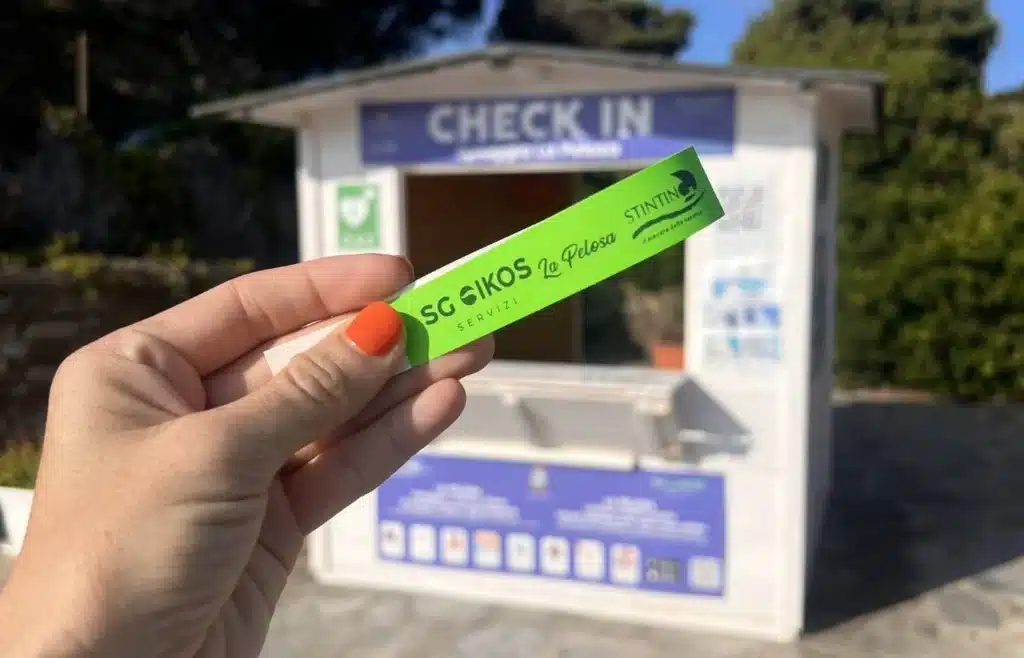Mano sosteniendo la pulsera verde de control de acceso tras hacer la reserva para la playa de La Pelosa.