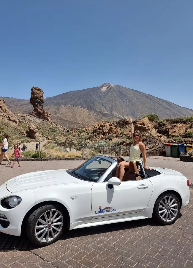 Mujer sentada en un descapotable blanco con el volcán Teide de fondo.