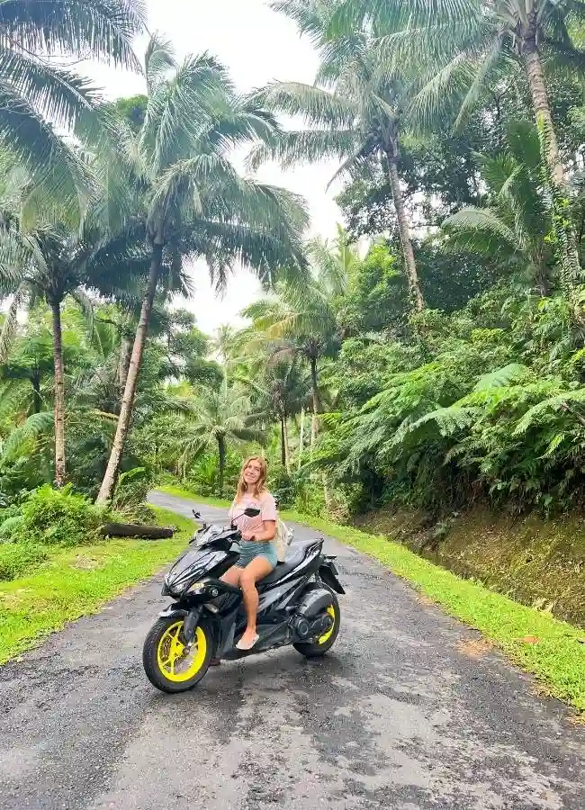 Mireia conduciendo una moto por una carretera rodeada de palmeras.