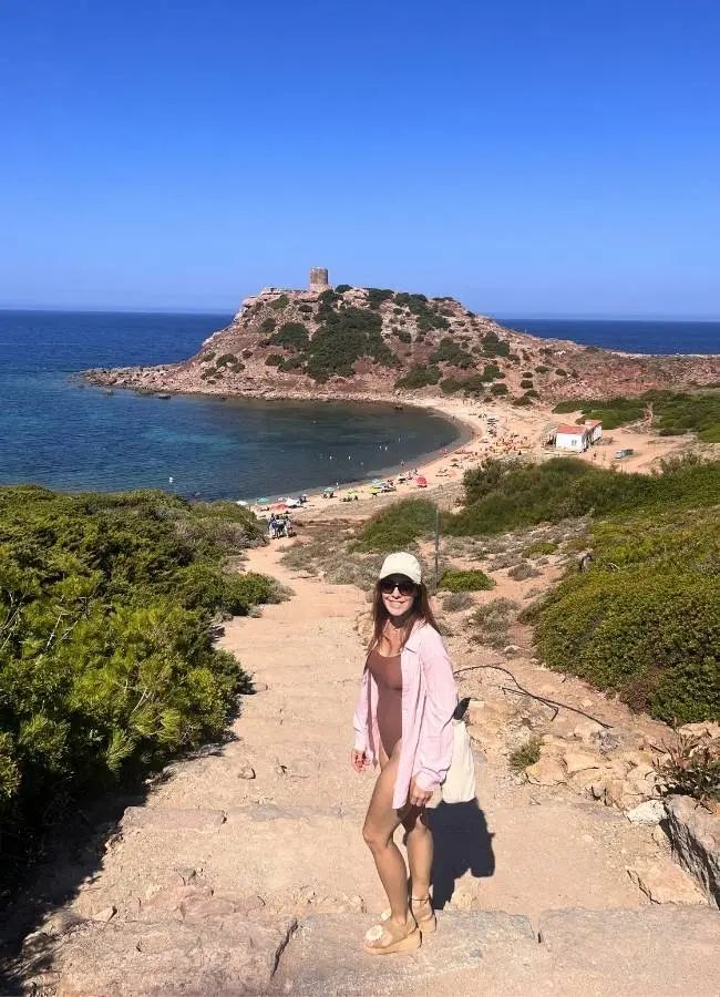 Mireia caminando por un sendero de tierra hacia una torre de vigía en el litoral de Cerdeña.