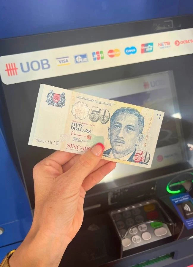 Mano sosteniendo billetes de dólares de Singapur tras sacarlos de un cajero.