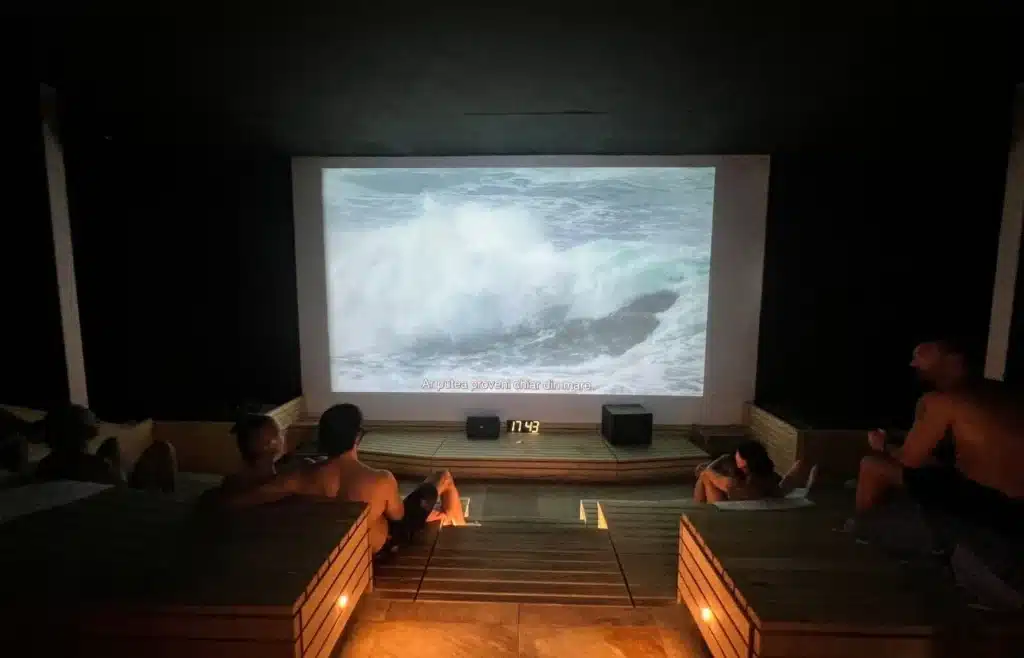 Personas relajándose en spa oscuro viendo olas proyectadas.