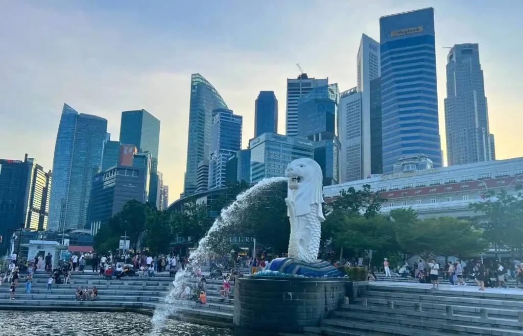 Estatua Merlion de Singapur con rascacielos y gente al atardecer.