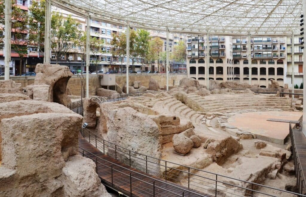 Ruinas de un teatro romano cubierto en un entorno urbano.