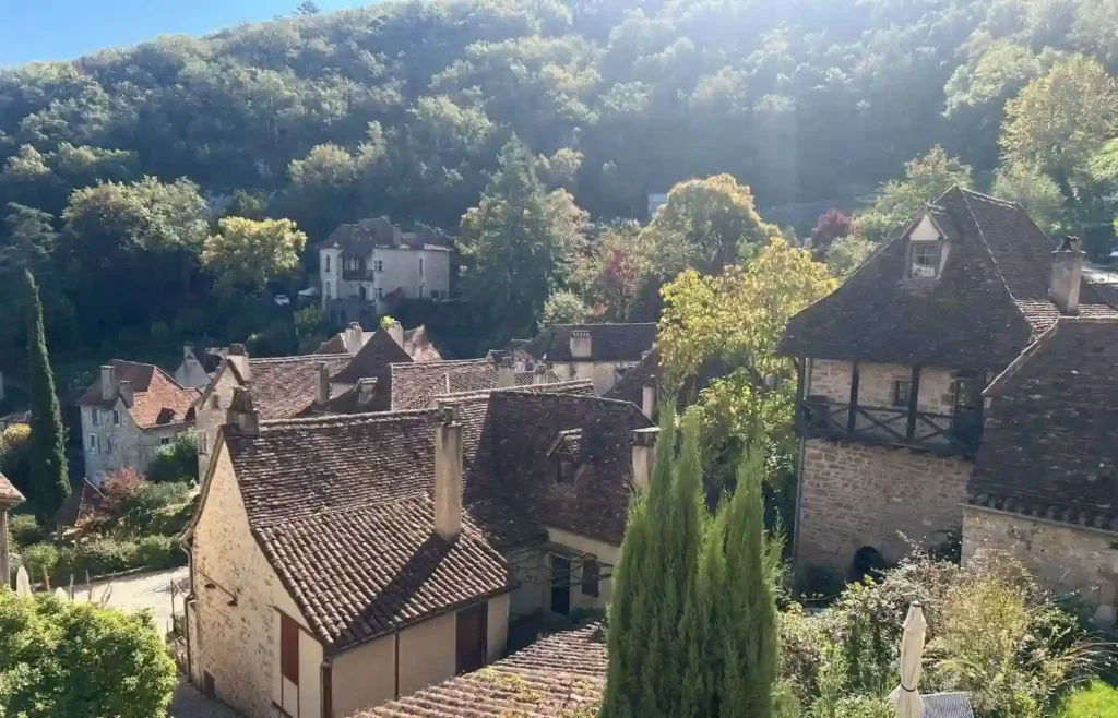 Pueblo medieval en valle boscoso con casas tejados marrones bajo sol.