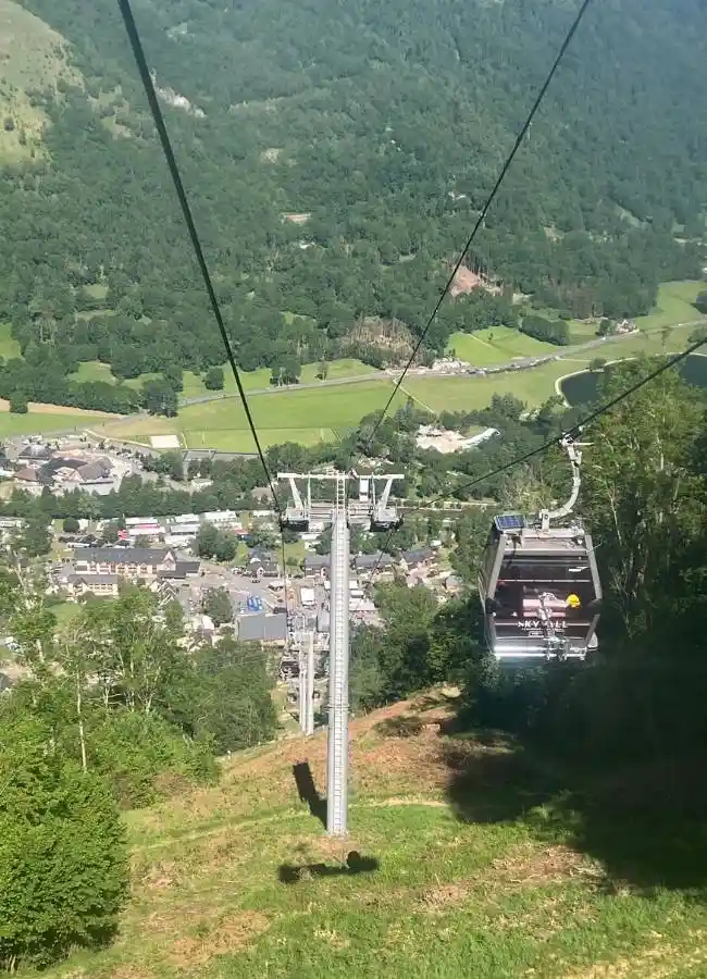 Telecabina descendiendo montaña con vistas a valle y pueblo.