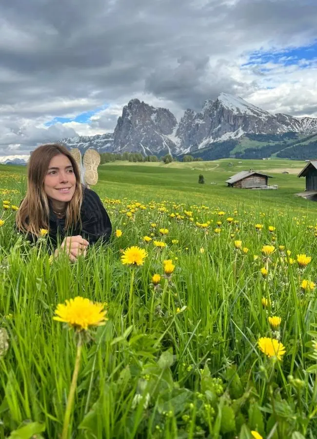 Mujer en campo de dientes de león, montañas nevadas, cabañas.