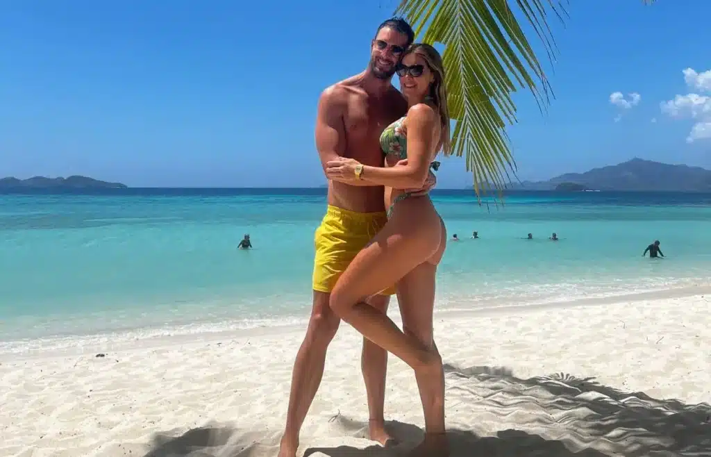 Pareja posando bajo la sombra de una palmera en una playa de arena blanca en Filipinas.