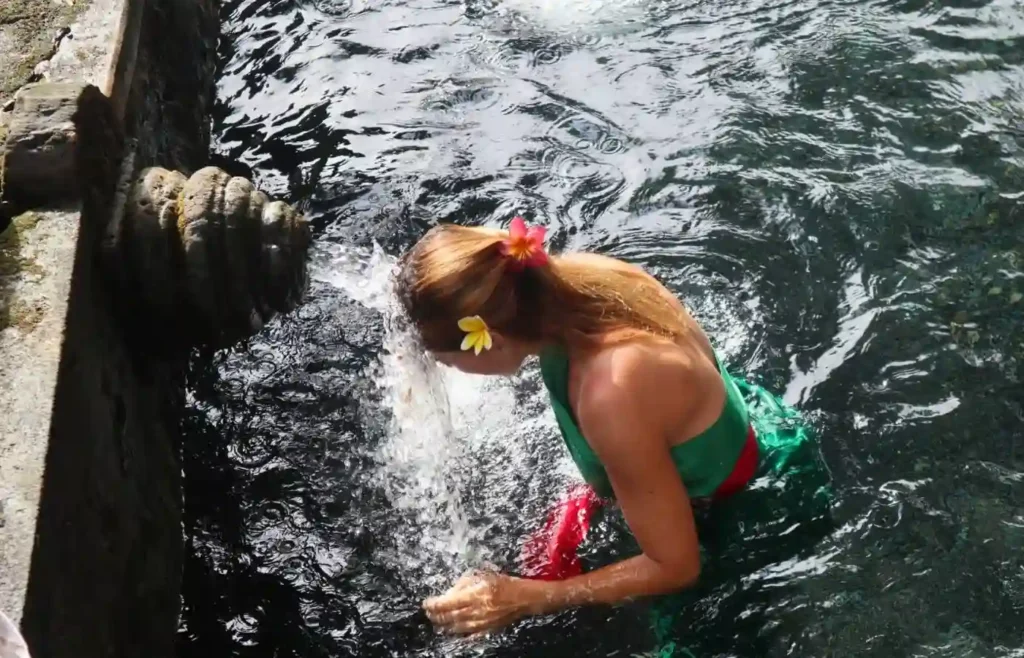 Mujer purificándose en templo balinés con agua sagrada y flores.