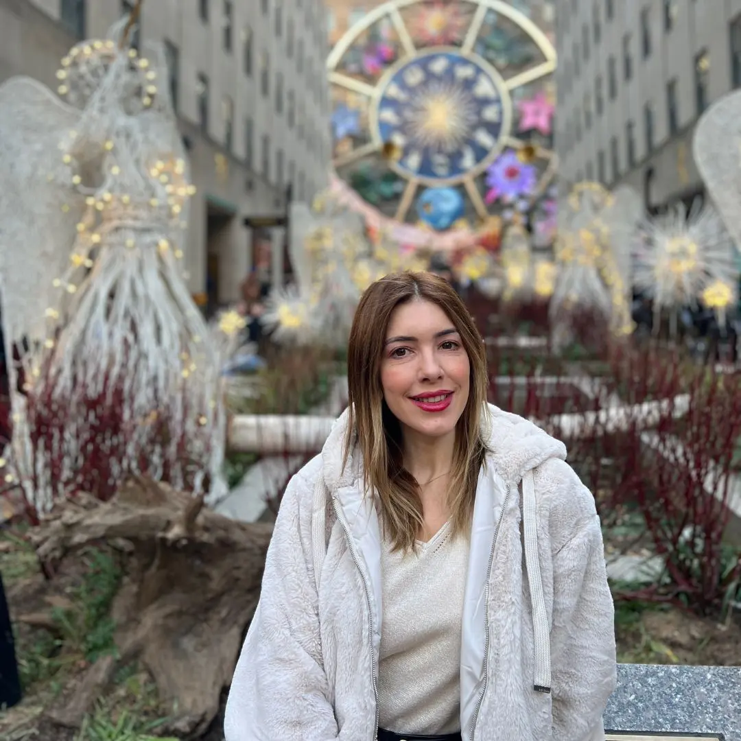 Chica posando frente al Rockefeller Center en Nueva York durante la Navidad con decoraciones luminosas.