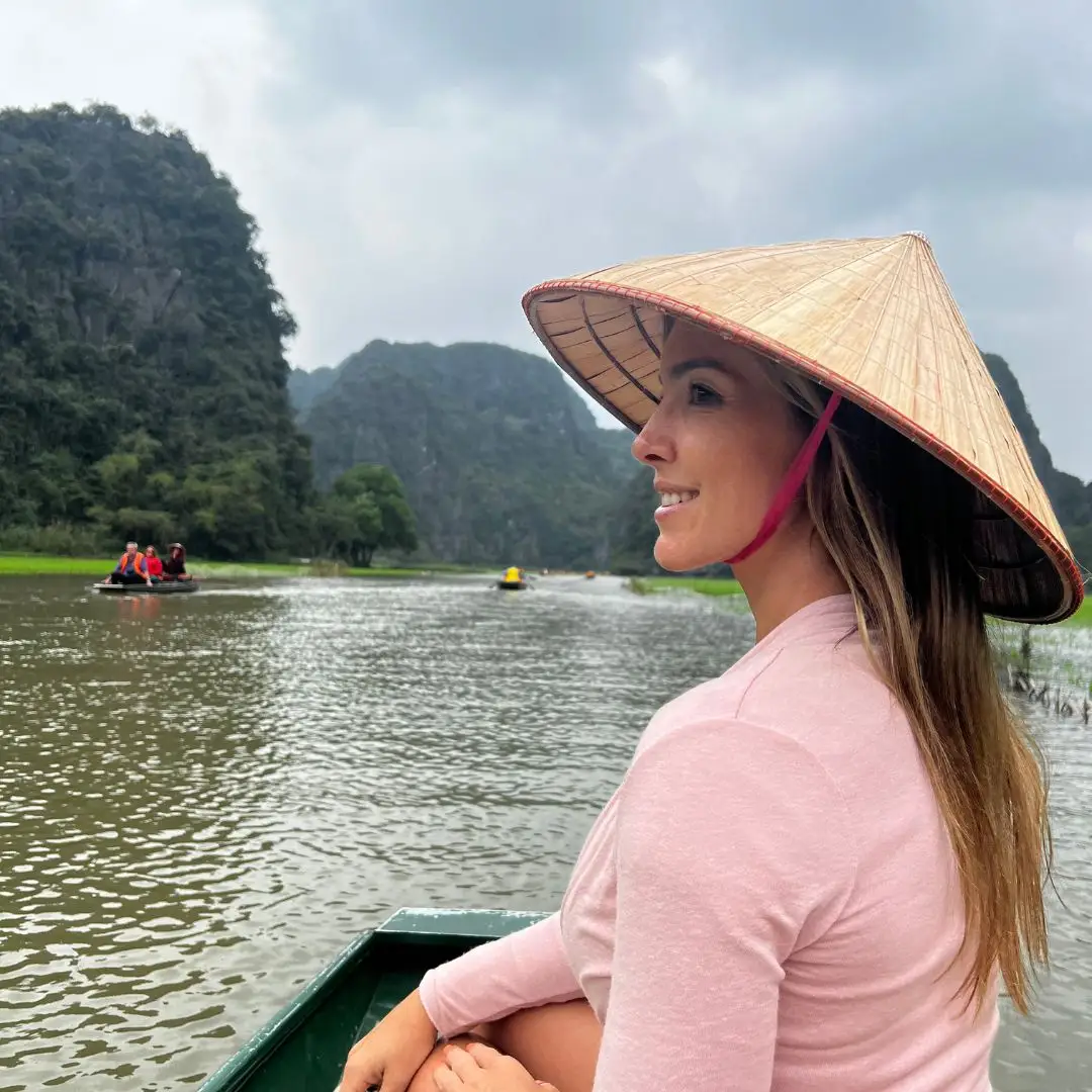 Mujer con sombrero tradicional vietnamita (Non La) disfrutando de un paseo en bote por los paisajes de Ninh Binh, Vietnam.