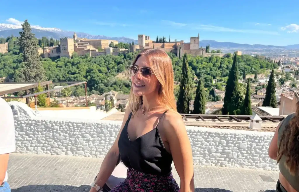 Mujer sonriendo en primer plano con el Palacio de Carlos V y la Alhambra de fondo.