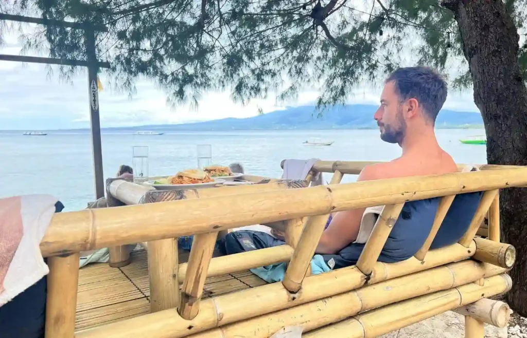 Viajero sentado en un banco de bambú frente al mar disfrutando de las vistas.
