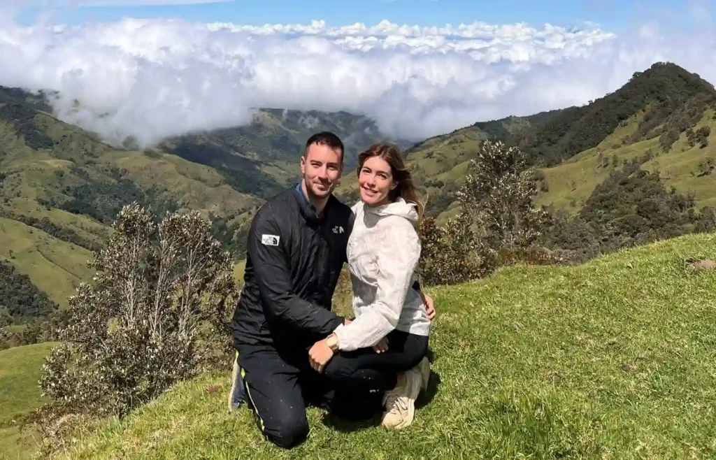 Pareja de viajeros agachados en una colina verde rodeados de palmas de cera en el bosque de Tochecito.
