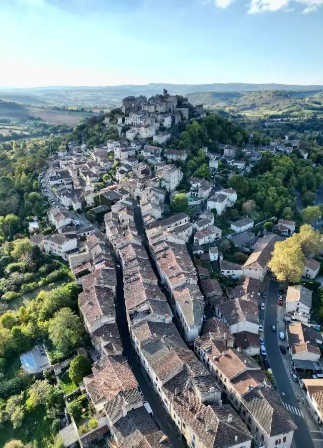 Vista aérea pueblo medieval en colina, casas con tejados, castillo.
