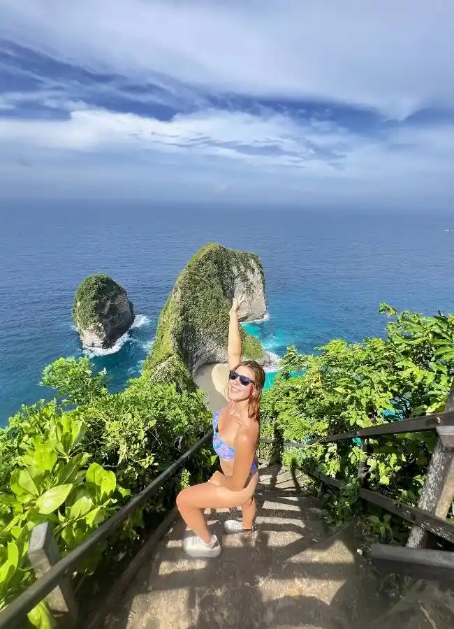 Mujer en bañador posa en escaleras con acantilados y mar azul.