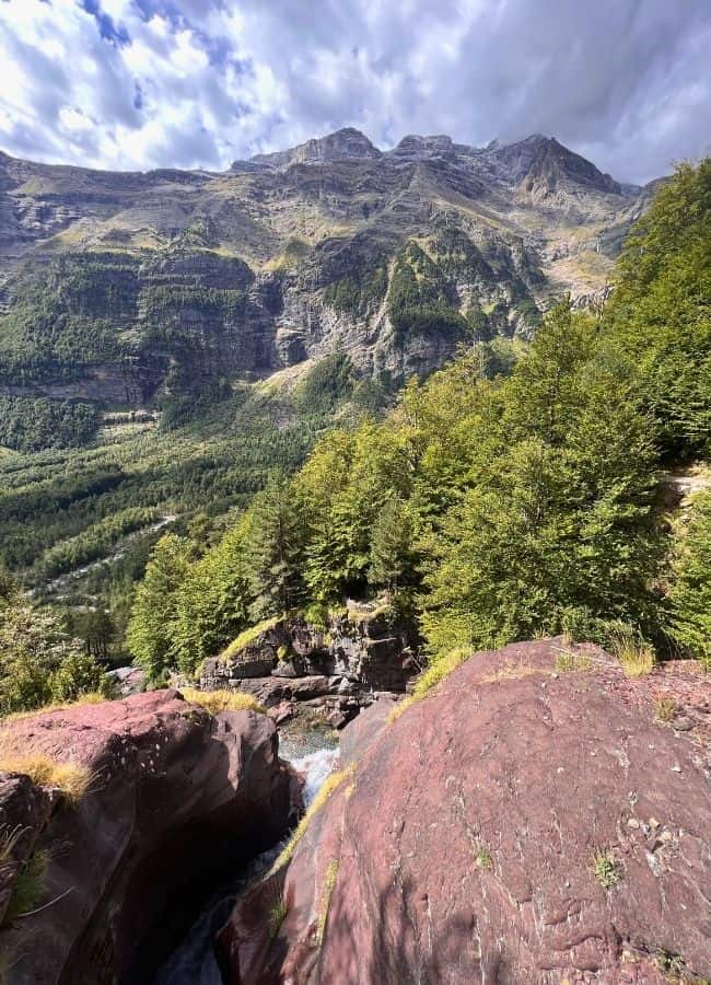 Paisaje de alta montaña con bosques verdes y picos rocosos desde el ascenso a La Larri.
